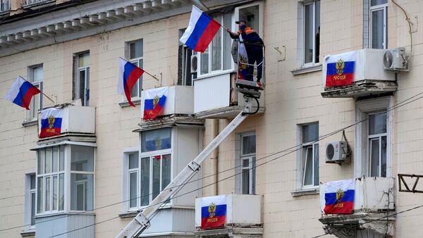 Arbeiter hängen russische Fahnen an einem Wohnhaus in der von Russland unterstützten und von Separatisten kontrollierten Volksrepublik Luhansk auf., © Uncredited/AP/dpa