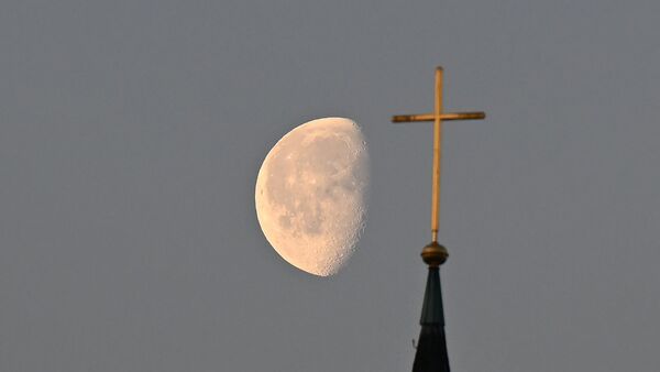 Der Mond steht im Morgenlicht hinter einem Kreuz auf einem Kirchturm., © Bernd Weißbrod/dpa/Symbolbild