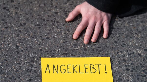 Ein Demonstrant hat sich während eines Protests auf einer Straße festgeklebt., © Sebastian Gollnow/dpa/Symbolbild