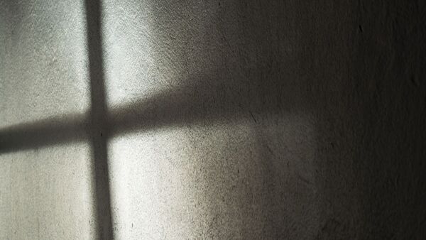 Ein Fenster wirft seinen Schatten auf die Wand. Es entsteht ein dunkles Kreuz., © Annette Riedl/dpa/Archivbild